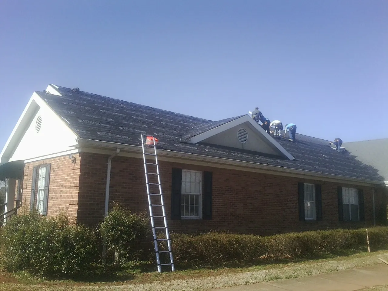 Crew tearing shingles off a brick ranch roof with a ladder set — Emergency Roof Repair work by our crew in Long Island City