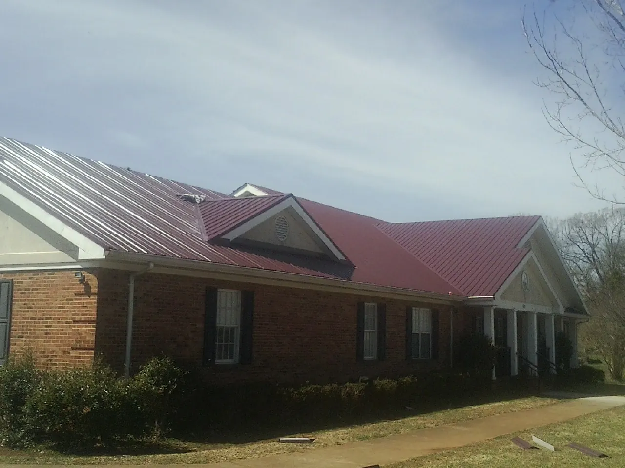 Red metal roof with gabled entries on a long brick building, from a Hail Damage Roof Repair job in Long Island City