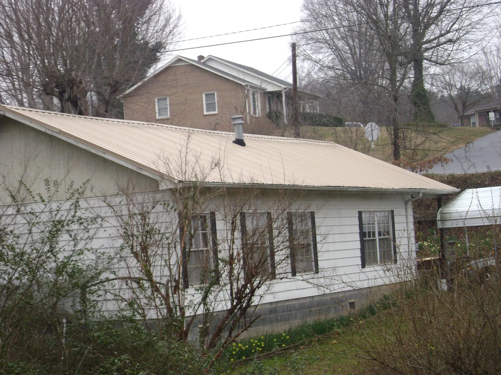 Tan metal roof on a white sided house set into a hillside — Commercial Roofing by Roofing Brothers in Long Island City