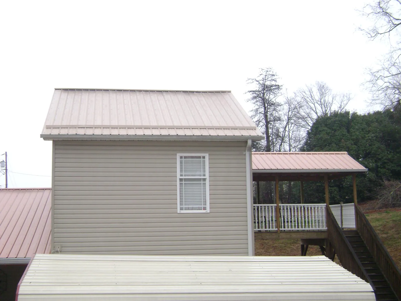 Tan metal roofs on a two story addition and attached porch, from a Roof Replacement job in Long Island City